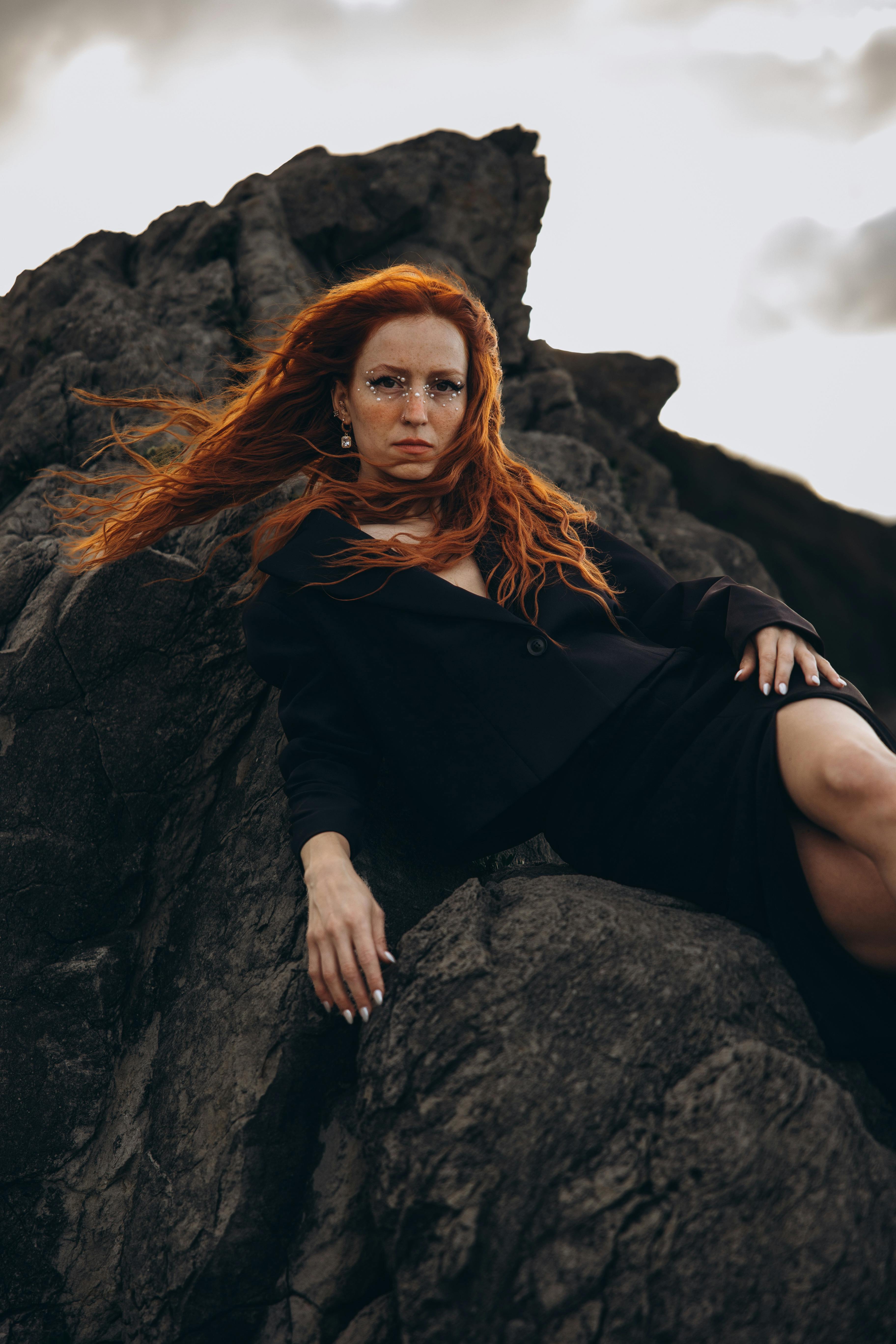 a woman with red hair sitting on a rock