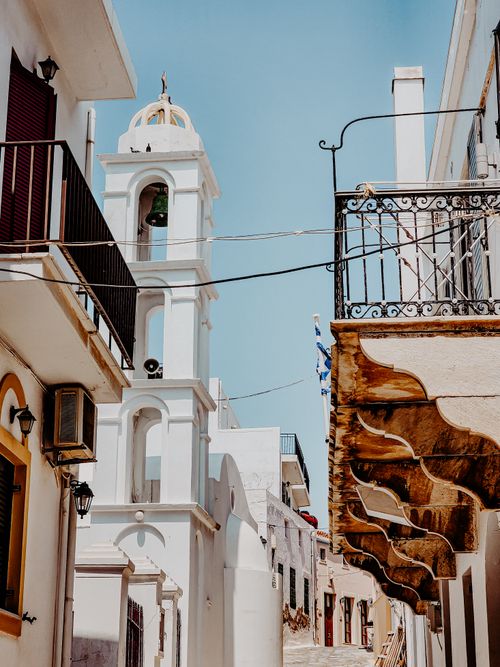 Free Picturesque Mediterranean alley featuring a white bell tower under a clear blue sky. Stock Photo
