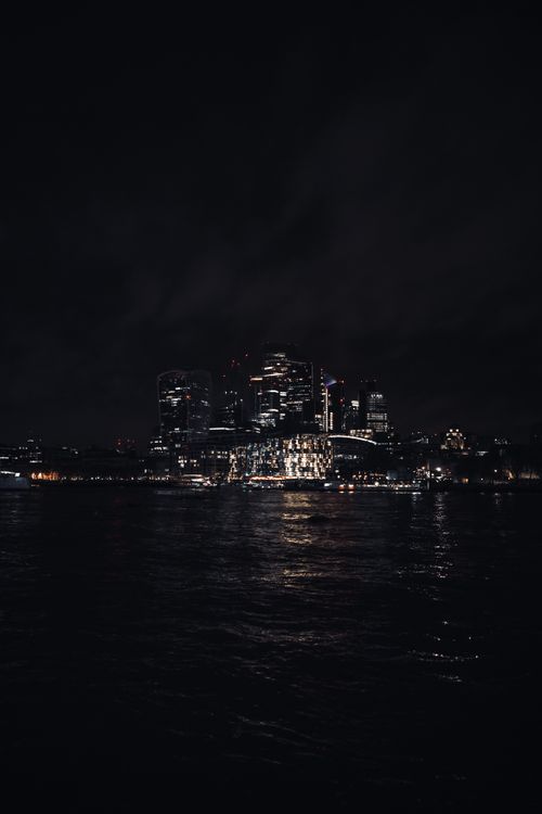 Free Illuminated skyscrapers of London's skyline reflecting on the River Thames at night. Stock Photo