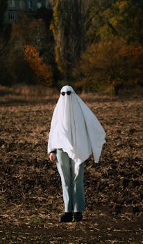 Person in ghost costume with sunglasses stands in a fall field.