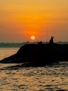 Silhouette of fishermen at sunset on Passagem Beach, Brazil with vivid orange sky and tranquil sea.