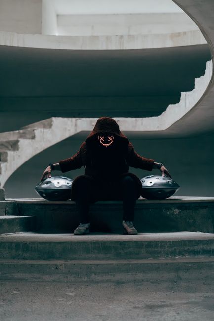Mysterious figure wearing a neon mask sitting at twilight on concrete stairs in Amantea, Italy.