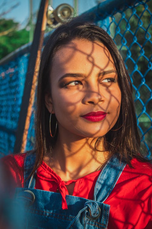 Free Woman Smiles and Leans Beside Blue Painted Chain-linked Fence Stock Photo