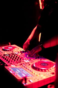 DJ spinning at a nightclub with vibrant red lighting and dynamic sound mixers.