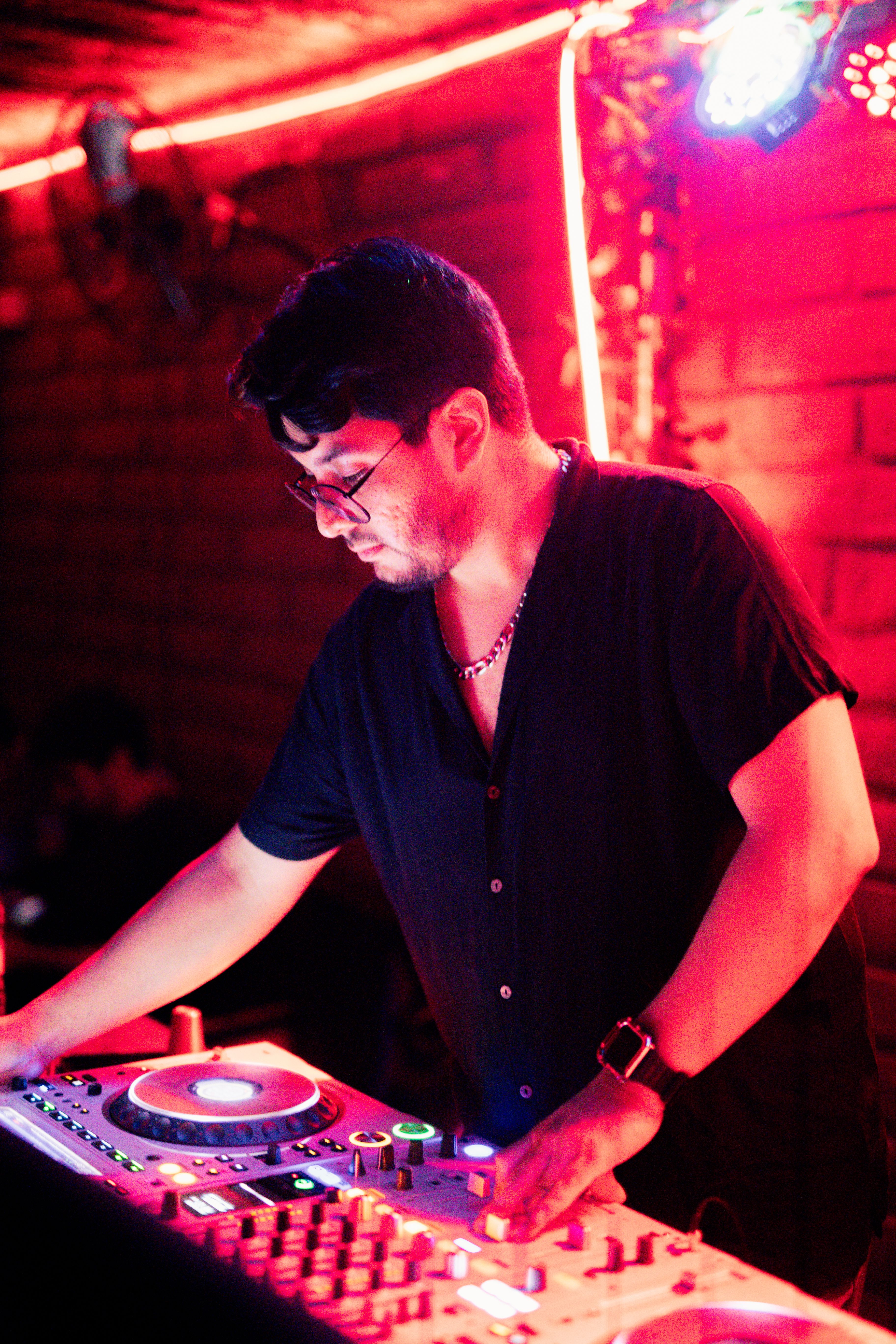 DJ mixes tracks in vibrant red-lit nightclub setting, creating energetic atmosphere.