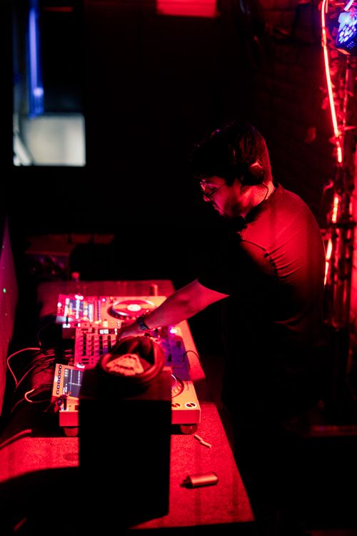 Free DJ playing music with sound mixer and speakers under red lights at nightlife event. Stock Photo