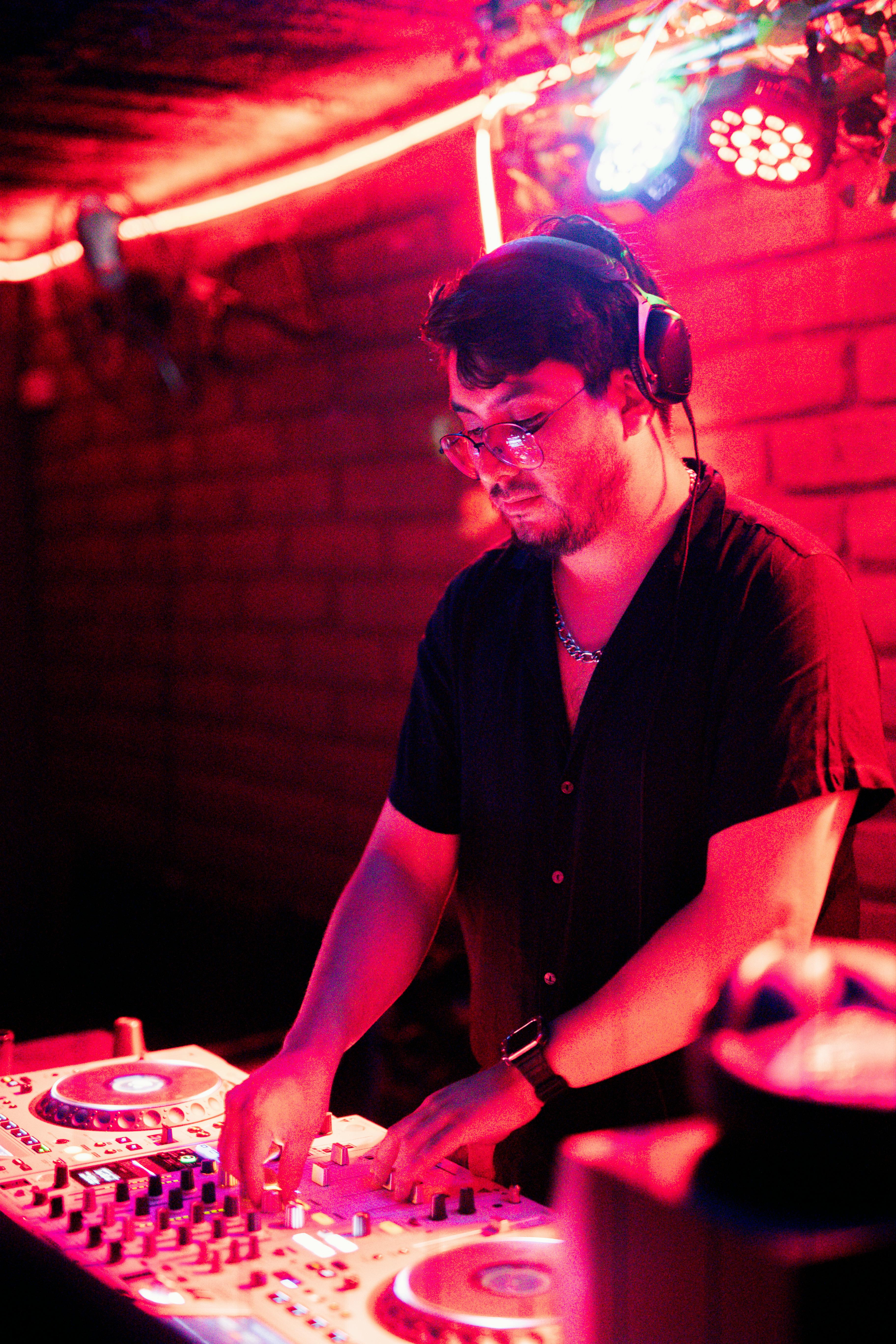 A DJ skillfully mixes music at a nightclub with vivid red and purple lighting, creating a vibrant atmosphere.