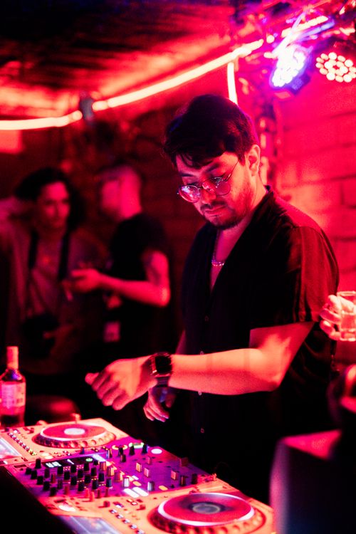 Free DJ engrossed in seamless mixing at a lively nightclub party with pink neon lights. Stock Photo