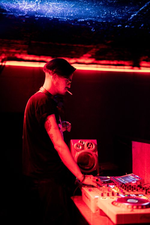Free DJ spinning tracks in a nightclub with vibrant red lights, surrounded by music equipment. Stock Photo