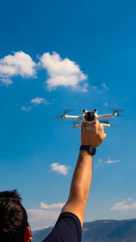 A person holding a drone with mountains and a clear blue sky in the background.