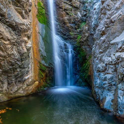 Free A picturesque waterfall cascading into a serene pool surrounded by rocky cliffs. Stock Photo