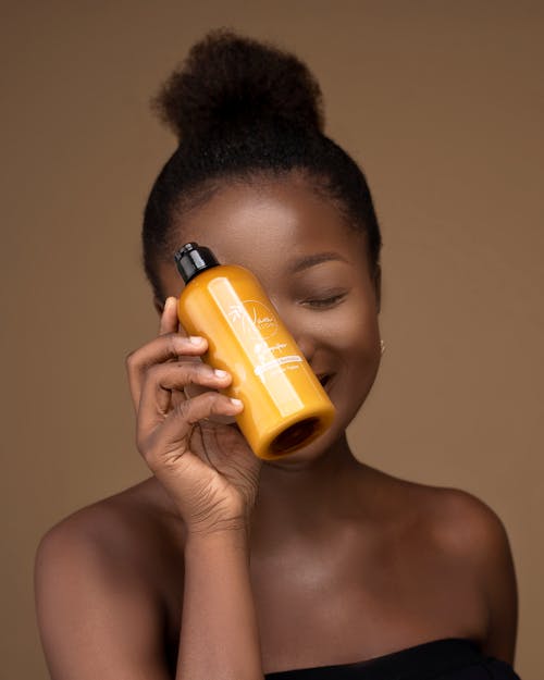 Young Model Smiling From Behind a Bottle of Beauty Product She is Holding