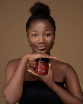 Elegant studio portrait of a woman holding a cosmetic jar with a neutral background.