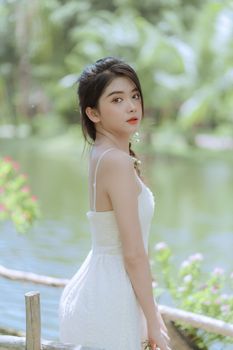 Charming portrait of a woman in a white dress posing gracefully by a tranquil lake in a lush park.