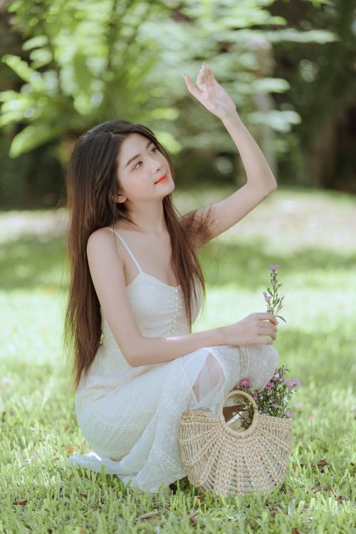 Free A young woman in a white sundress poses outdoors, basking in the summer sunlight. Stock Photo