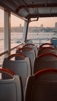 View from an empty ferry with seats facing the Istanbul coast during sunset, highlighting the serene sea view.