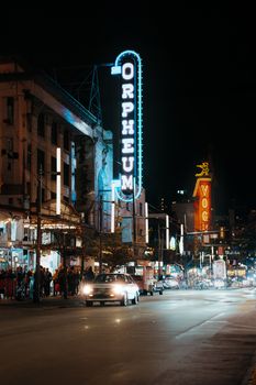 Illuminated Orpheum Theatre sign with bustling city street at night in Vancouver.