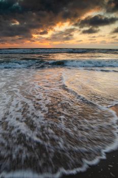 Captivating sunset over the ocean with waves hitting the shore and dramatic clouds.
