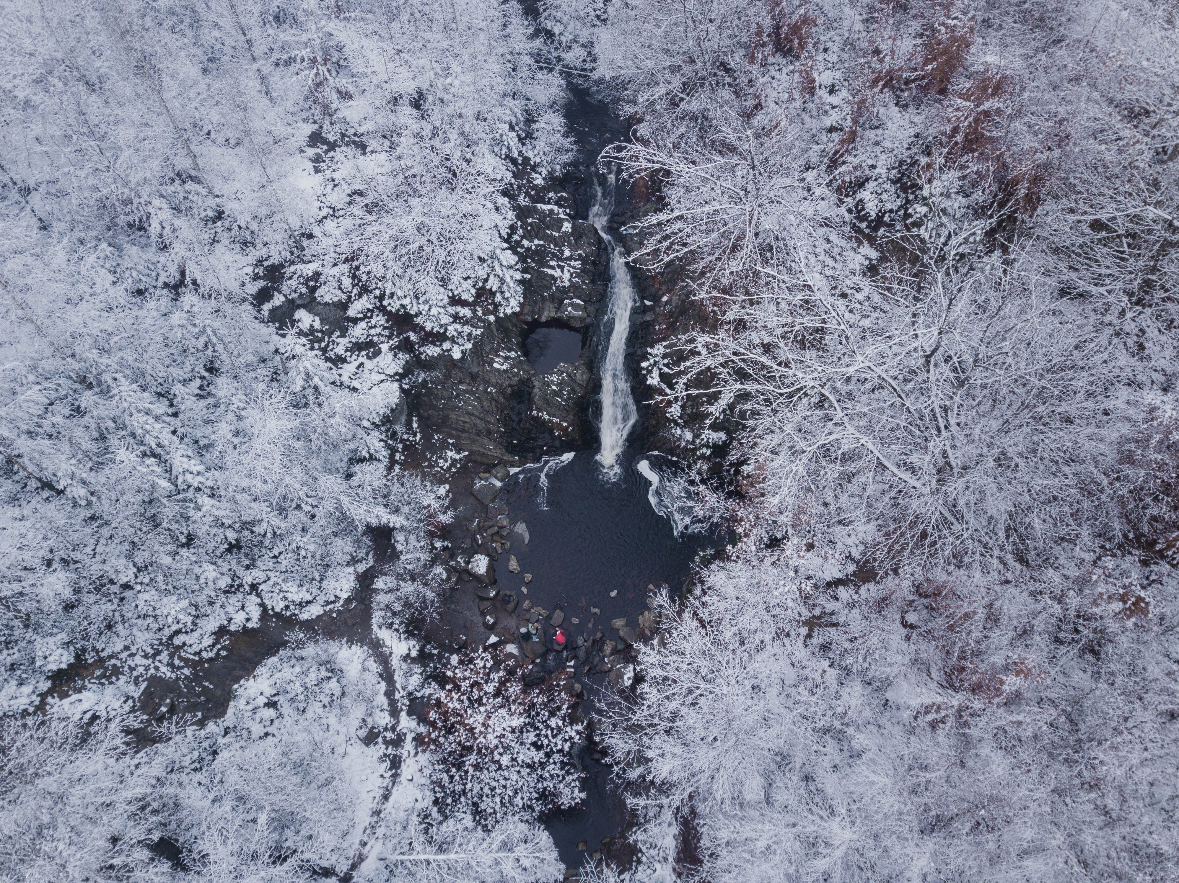 A breathtaking aerial view of a frozen waterfall surrounded by a snow-covered forest.