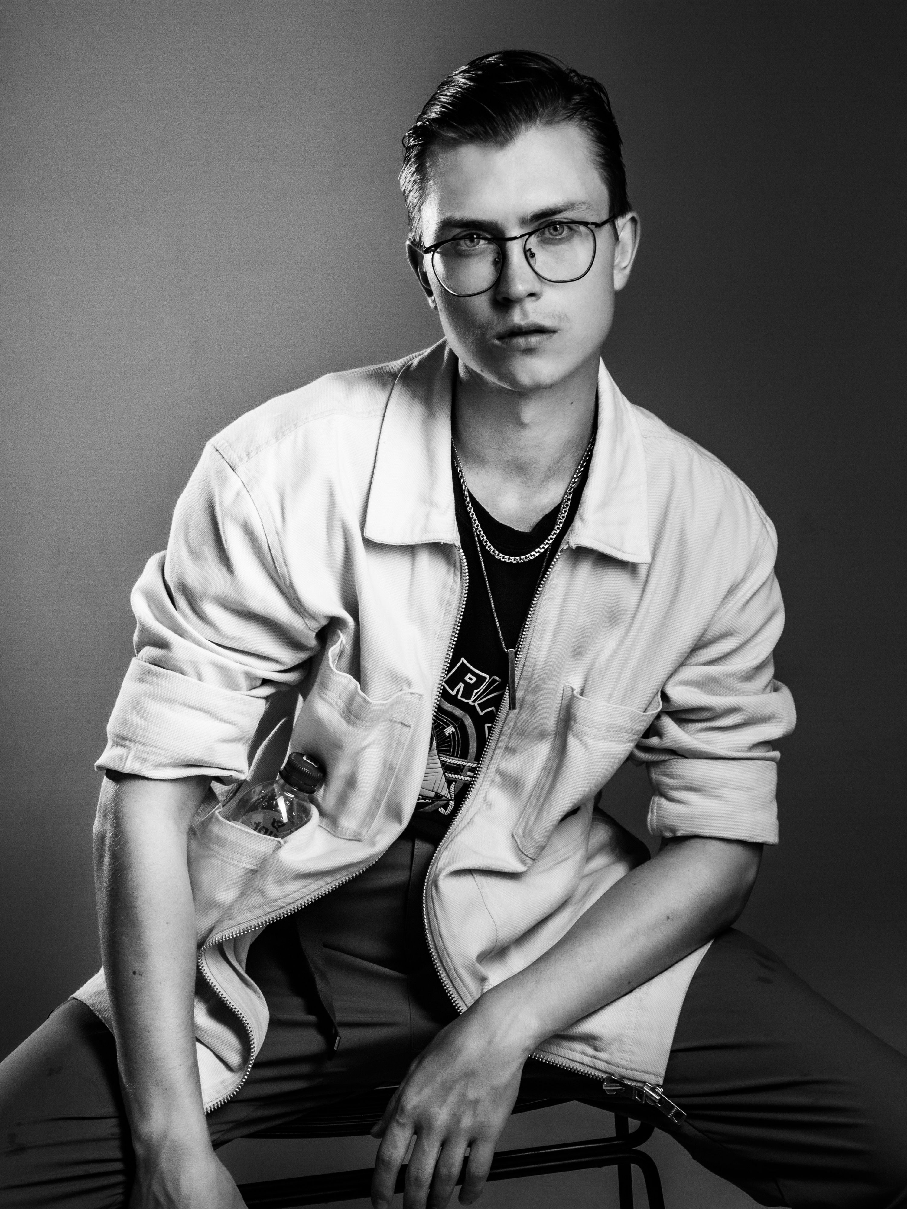 Black and white studio portrait of a stylish young man sitting with confident expression.