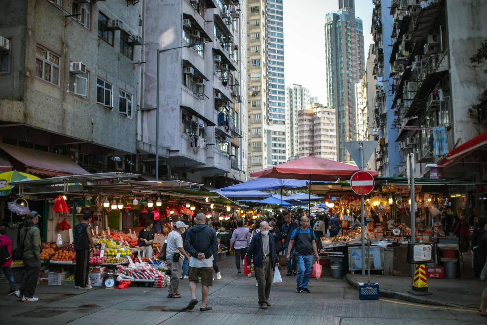 Busy outdoor Hong Kong market with crowds and high-rise buildings in the background
