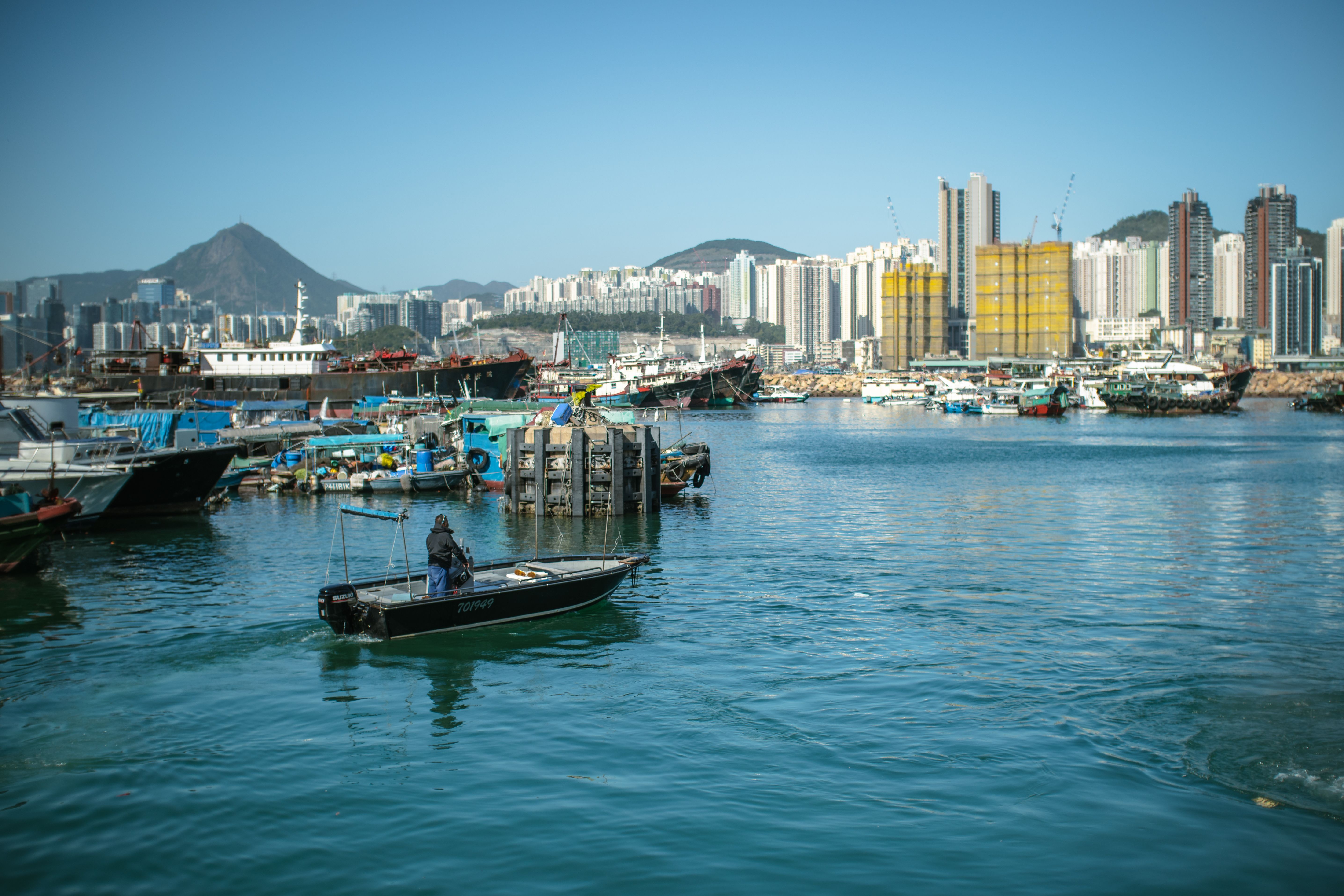 A bustling Hong Kong harbor scene featuring boats, skyscrapers, and clear blue skies.
