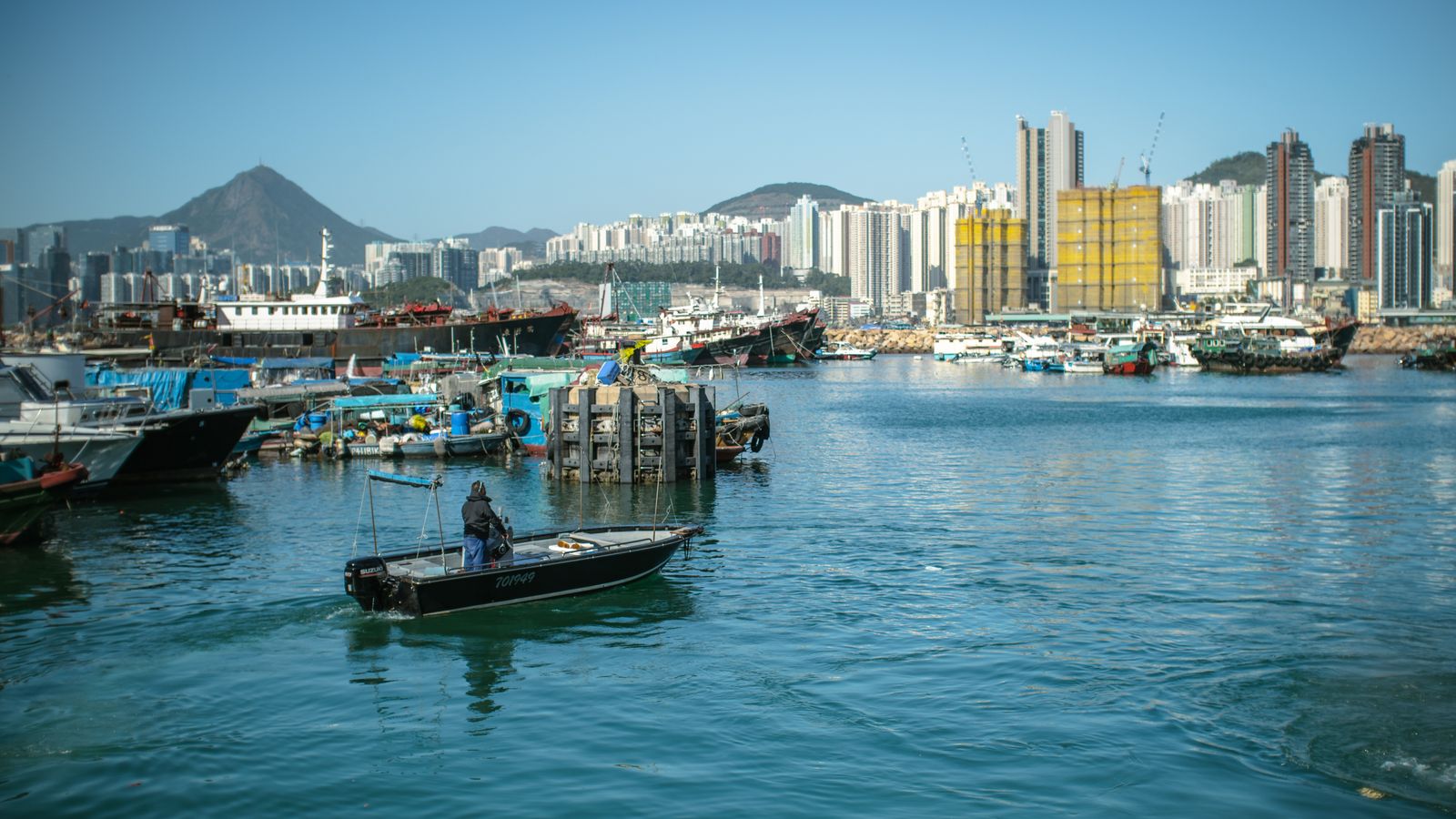 A bustling Hong Kong harbor scene featuring boats, skyscrapers, and clear blue skies.