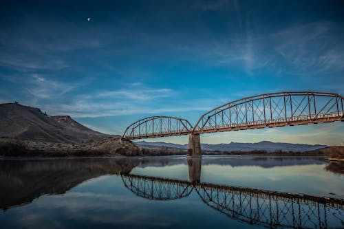 青い空の下の澄んだ川の水に反射する茶色の金属橋