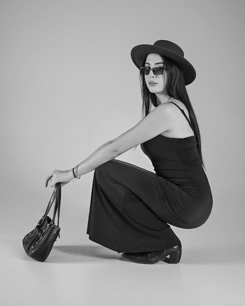 Elegant Woman in Black Dress with Hat Crouching in Studio