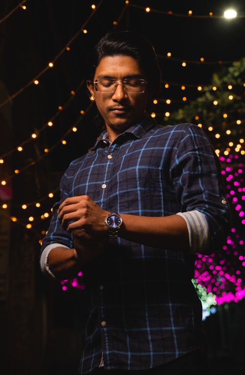 Free A man adjusting his watch under colorful string lights at night, creating a festive ambiance. Stock Photo