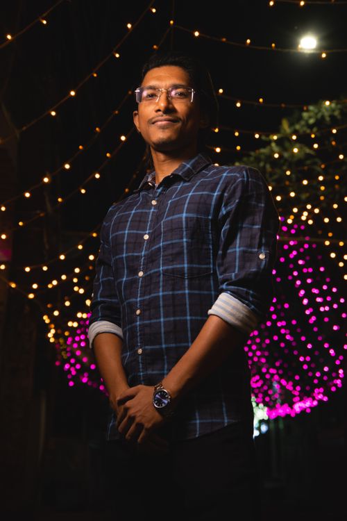 Free A man wearing glasses and a checkered shirt stands confidently under night lights. Stock Photo