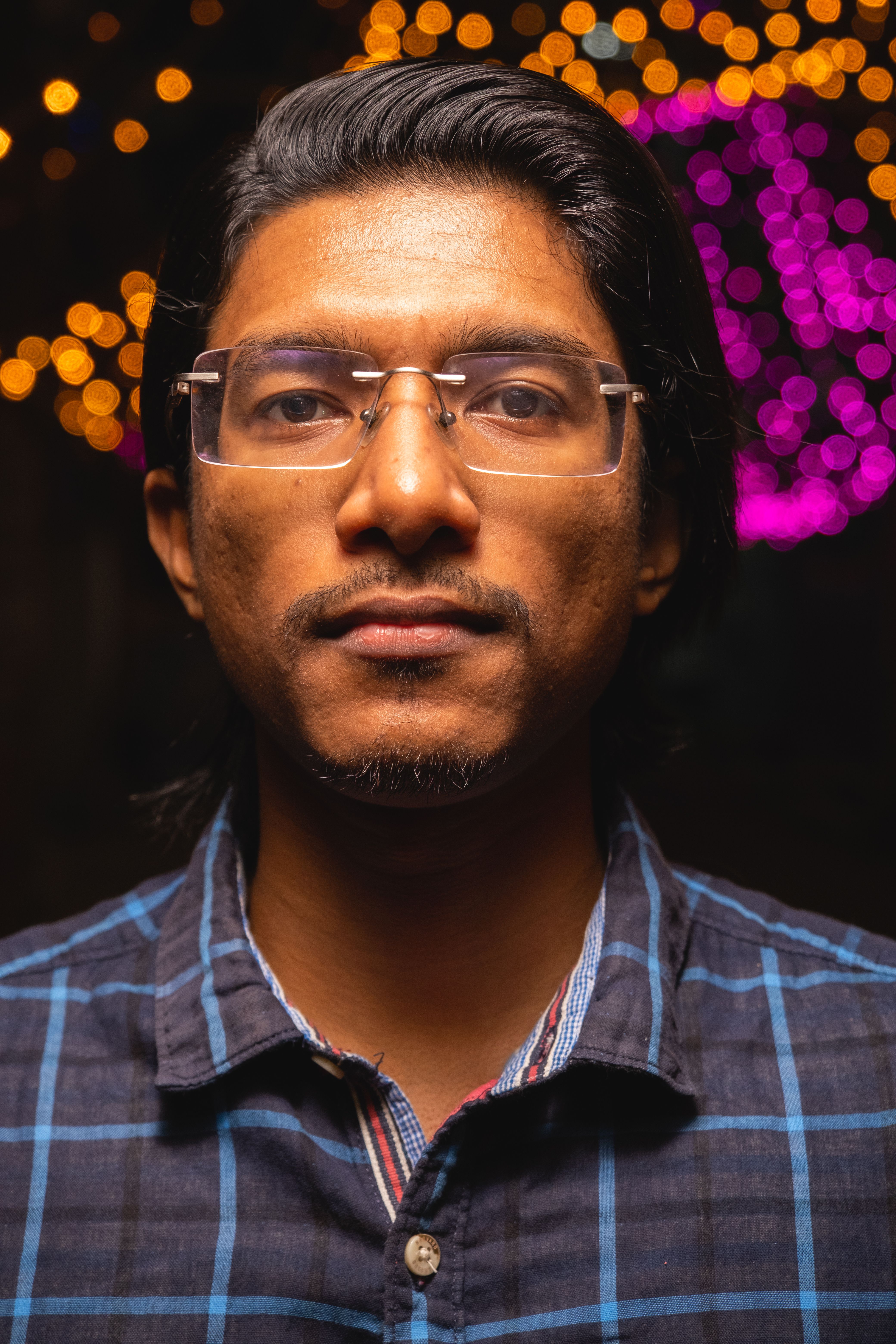 Close-up portrait of a man wearing glasses with bokeh lights in the background, capturing a vivid night scene.