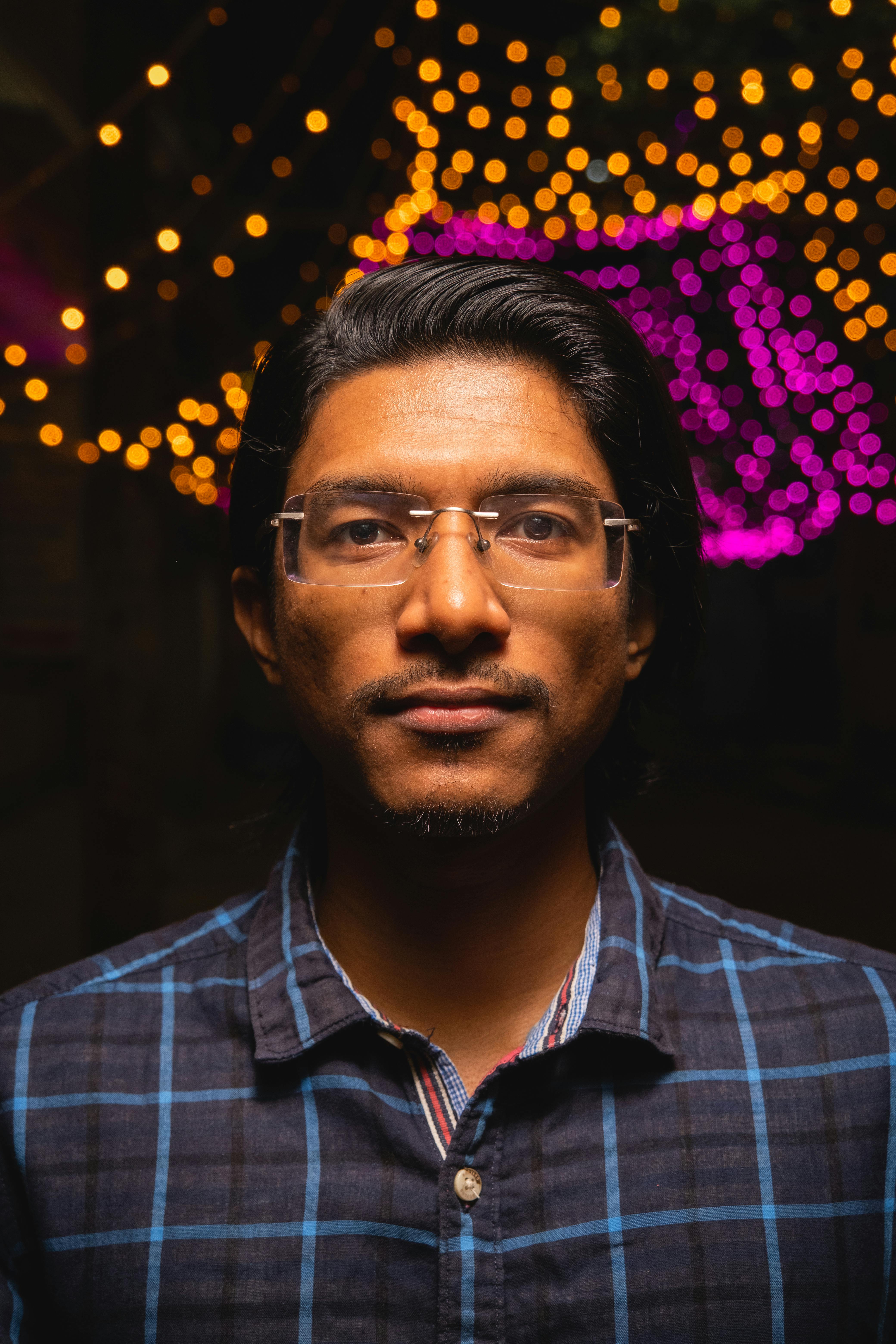 Close-up of a man with eyeglasses and festive lights, showcasing an urban portrait style.