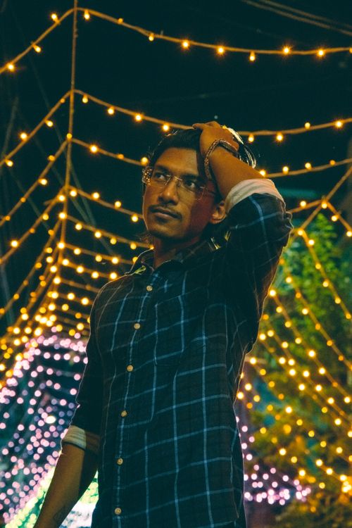 Free Young man adjusting hair under colorful string lights, creating a festive atmosphere. Stock Photo