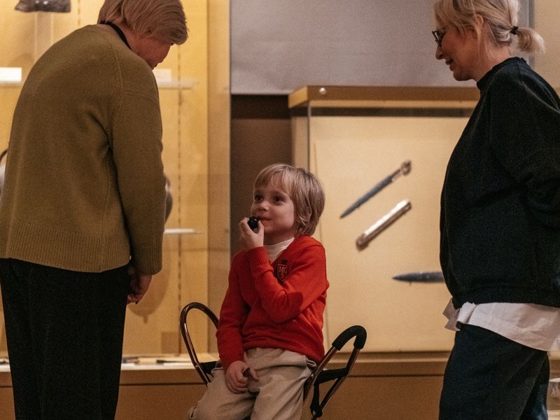 A child in red sweater sitting in a museum with two adults engaged in conversation - homeschool history field trips