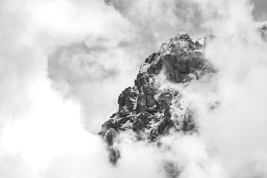 A dramatic black and white view of a misty alpine mountain peak hiding in clouds.