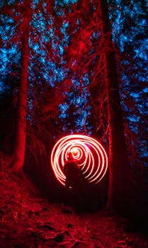 A lone traveler creates vibrant red light swirls in a dark, mystical forest setting.