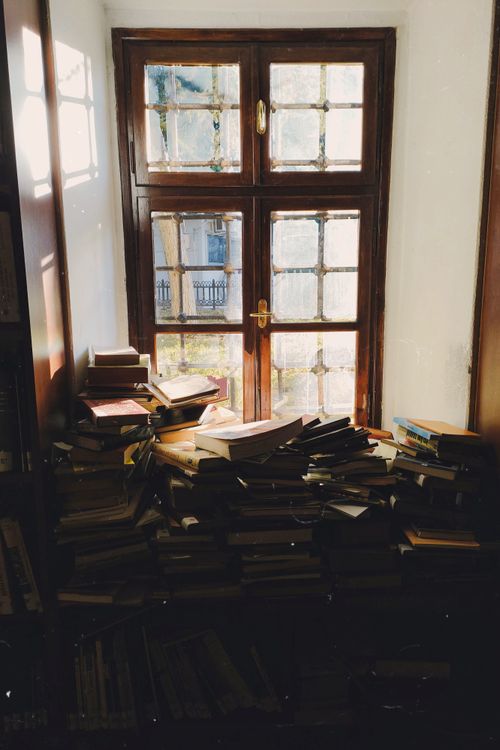 Free Sunlit window and stacked books create a cozy reading environment in a quiet room. Stock Photo