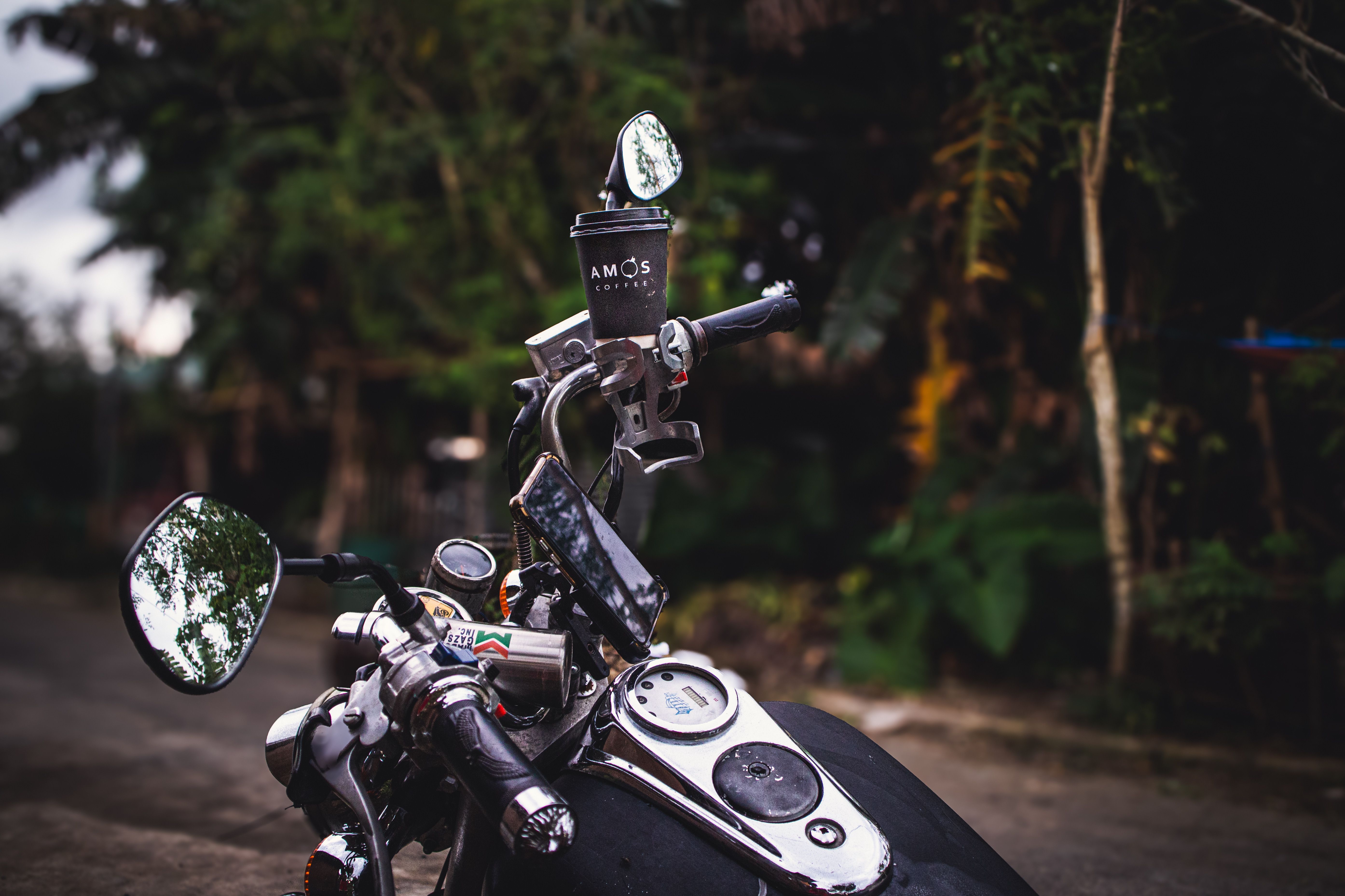 Close-up of a motorcycle with a coffee cup mounted on the handlebar in an outdoor setting.