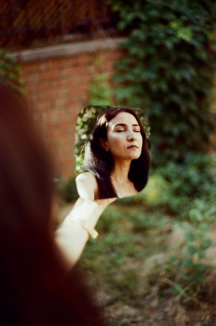 A serene portrait of a woman reflected in a mirror, surrounded by nature's greenery.