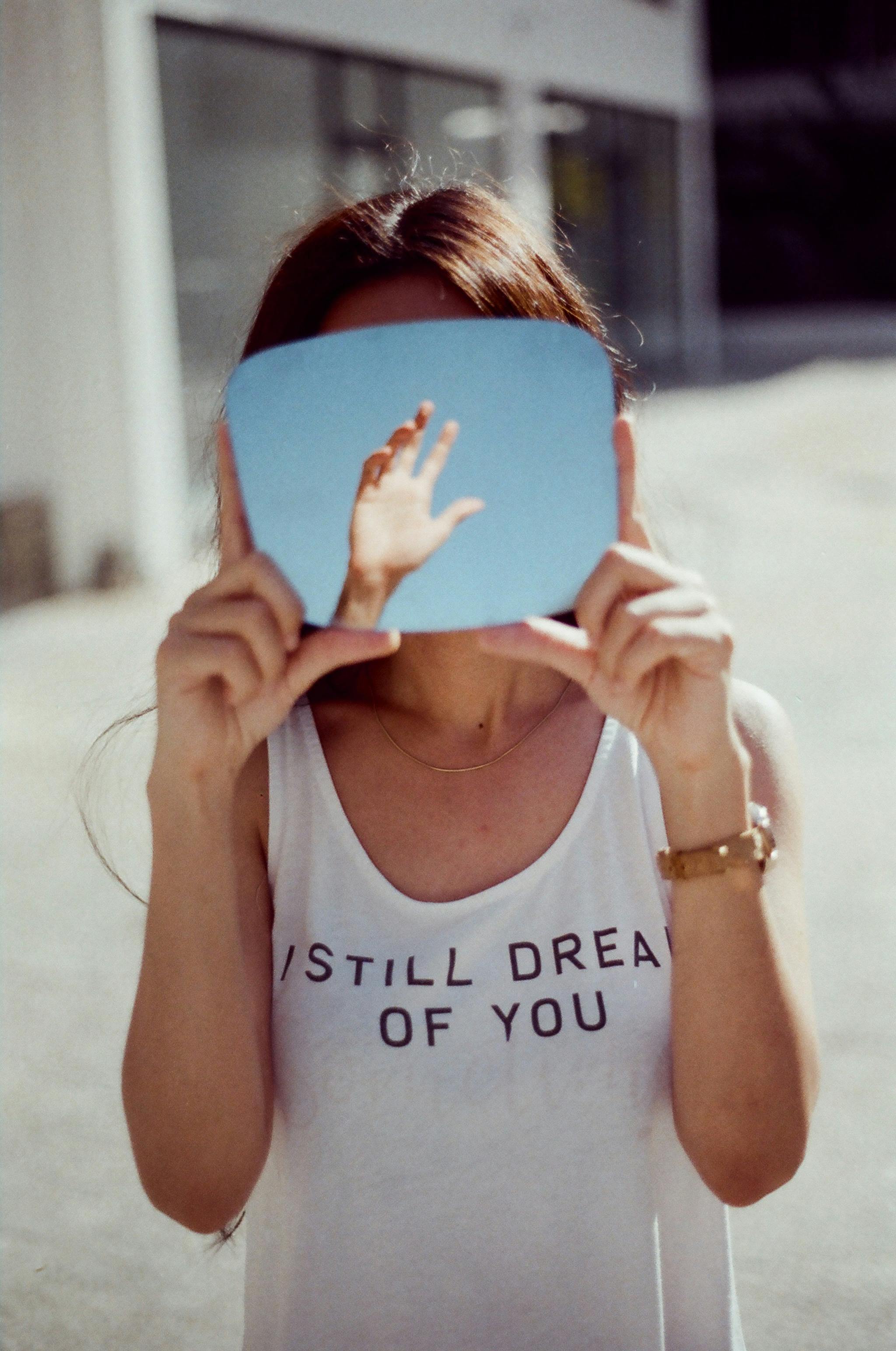Creative photo of a woman holding a mirror reflecting a sky and hand. Conceptual and intriguing.