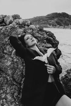 Artistic black and white portrait of a woman with a flower by a rocky seaside in Türkiye.