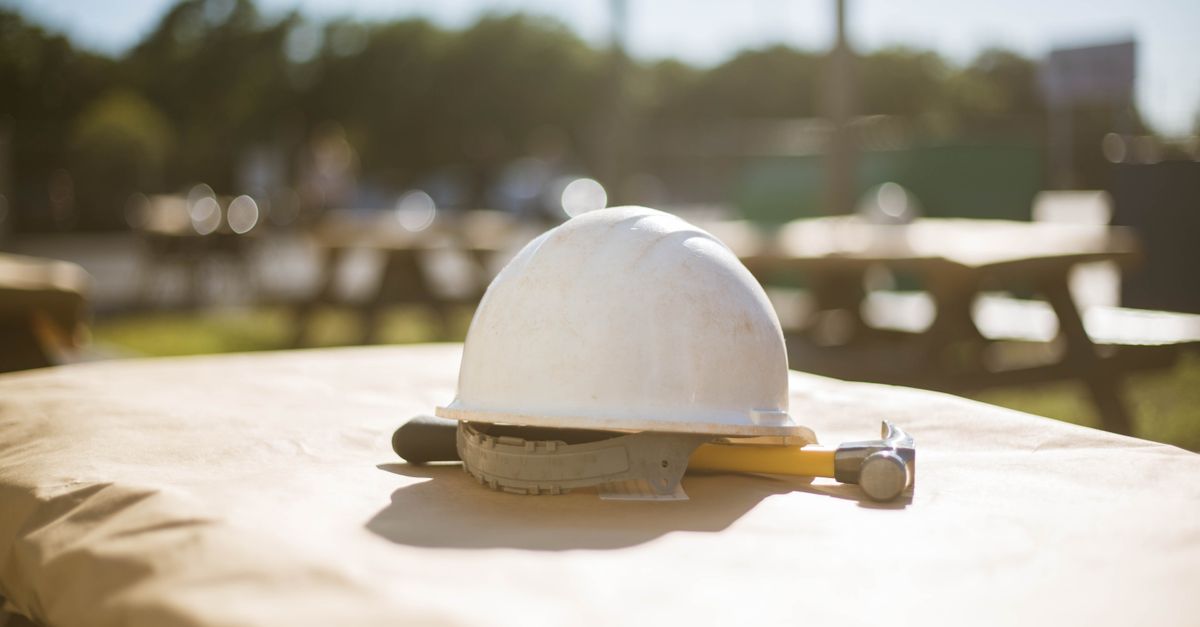White construction hard hat and hammer on a picnic table outside in sunny Pensacola, FL setting.