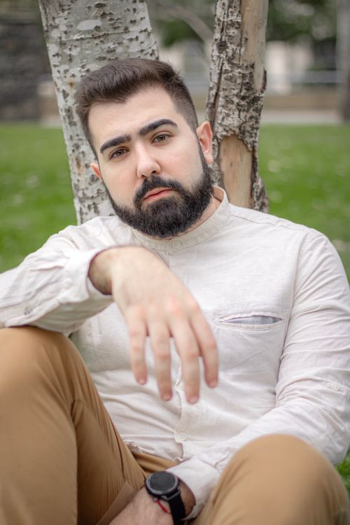 Free Bearded man in a white shirt seated outdoors with a relaxed pose, showcasing casual fashion Stock Photo