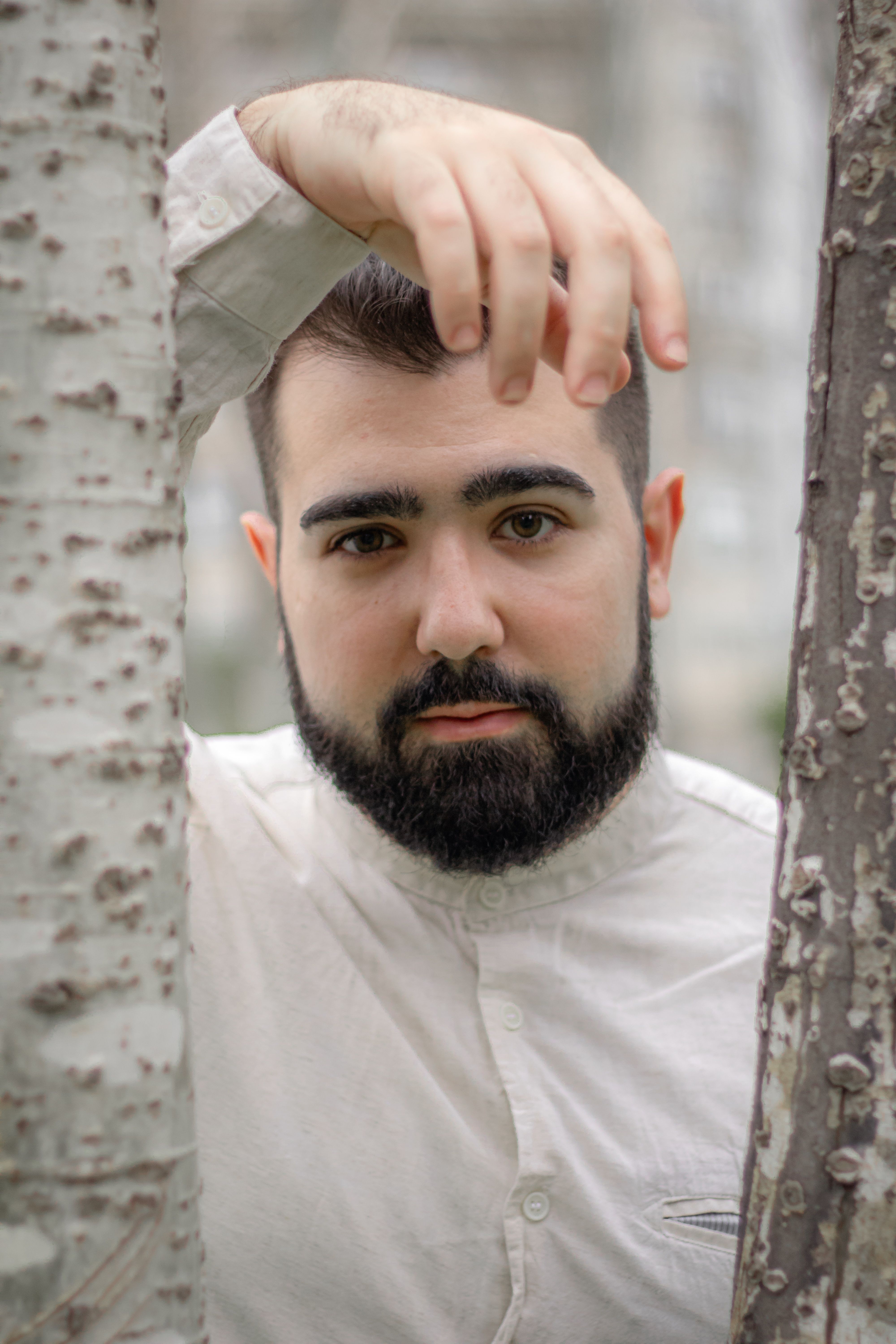 Close-up portrait of a man with a beard and mustache standing between tree trunks
