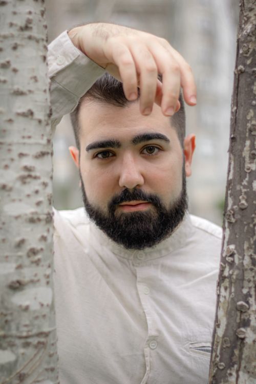 Free Close-up portrait of a man with a beard and mustache standing between tree trunks Stock Photo