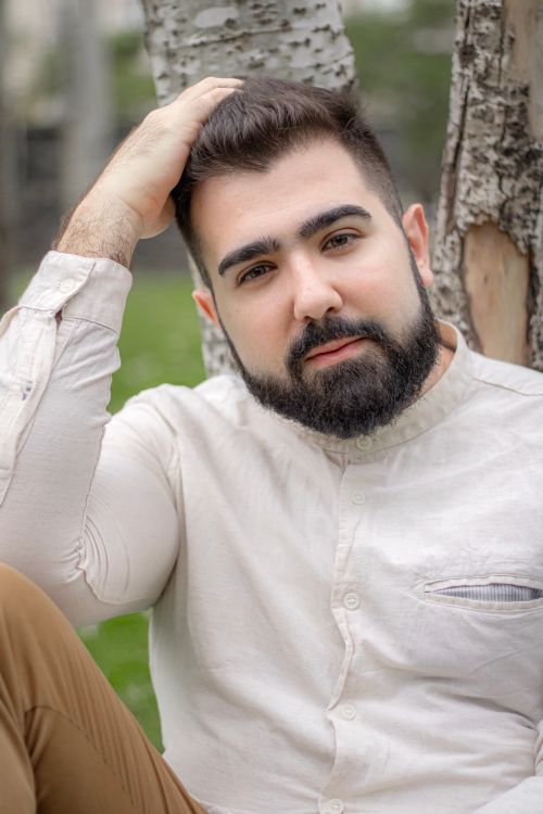 Free Relaxed portrait of a man with a beard and mustache sitting against a tree outdoors. Stock Photo