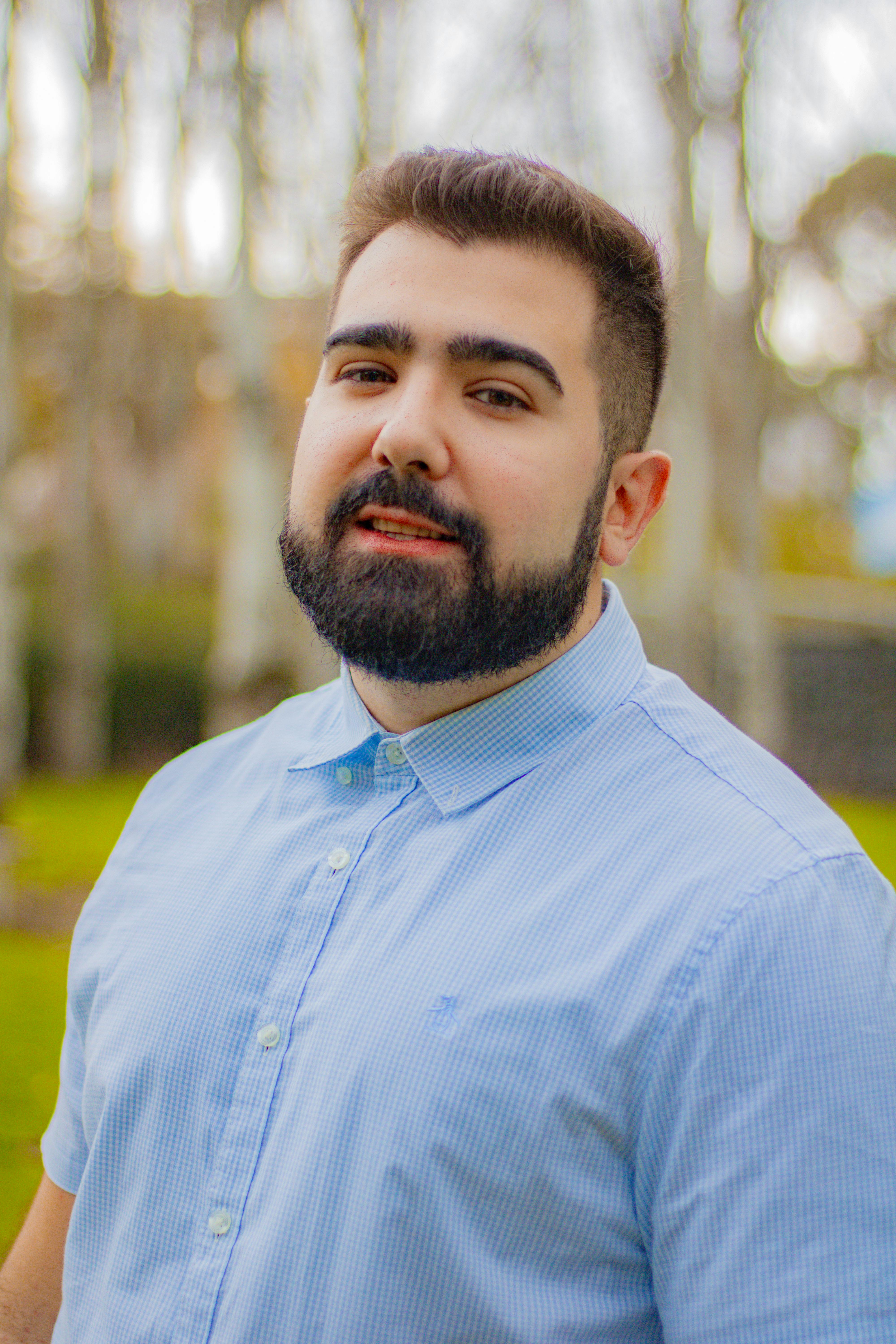 Stylish young man with a beard in a blue shirt enjoying a sunny day outdoors.