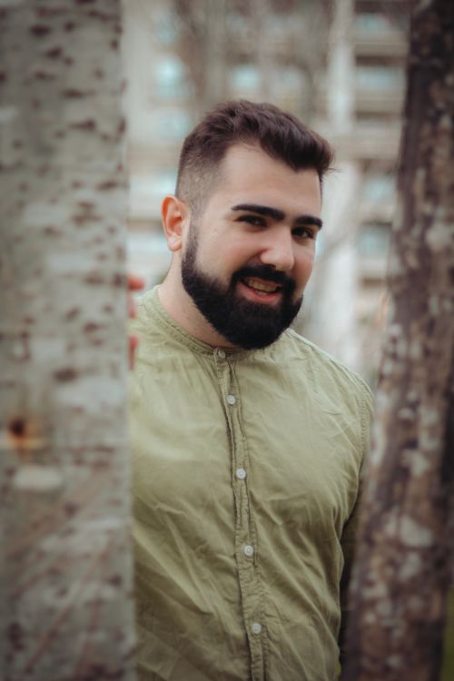 Free Portrait of a bearded man in a khaki shirt standing between trees outdoors. Stock Photo