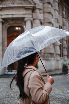 Woman holding a clear umbrella walking in a historic city street during rain.